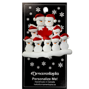 Family ornament with 9 white snowmen in red hats, gathered around a red maple leaf, on display backing card.