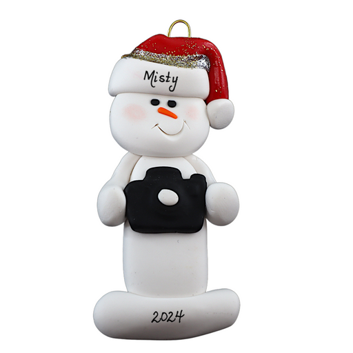 Ornament of white snowman in red hat holding a black camera, personalized with name.