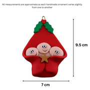 Ornament with triplet infant heads poking out of a red baby blanket, graphed to show size (7x9.5cm).