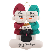 Ornament of snowman couple in red and green shirts and hats with black dog in Christmas hat, personalized with names.