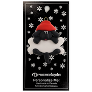 Ornament of black dog in red hat hanging on a white bone, on display backing card.