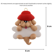 Ornament of tan dog in red hat hanging on a white bone, graphed to show size (6x8cm).