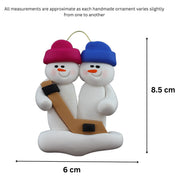 Family ornament with 2 white snowmen in bright hats, holding a hockey stick, graphed to show size (6x8.5cm).