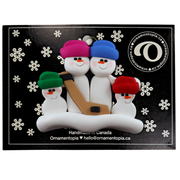 Family ornament with 4 white snowmen in bright hats, holding a hockey stick, on display backing card.