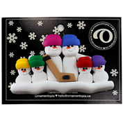 Family ornament with 6 white snowmen in bright hats, holding a hockey stick, on display backing card.