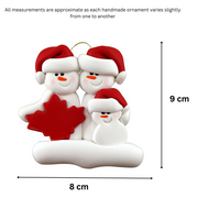 Family ornament with 3 white snowmen in red hats, gathered around a red maple leaf, graphed to show size (8x9cm).