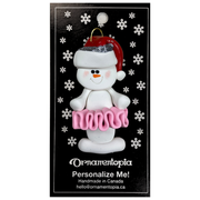 Ornament of white snowman in red hat wearing a pink tutu, on display backing card.
