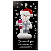 Ornament of white snowman in red hat holding a bingo card and dabber, on display backing card.