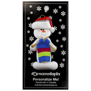 Ornament of white snowman in red hat holding an in-progress knitting project on knitting needles, on display backing card.