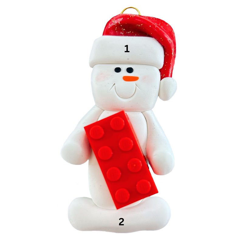 Ornament of white snowman in red hat holding a plastic building brick, numbered 1-2 for personalization.