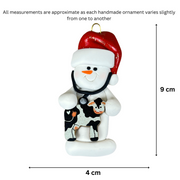 Ornament of white snowman in red hat holding a cow and stethoscope, graphed to show size (4x9cm).