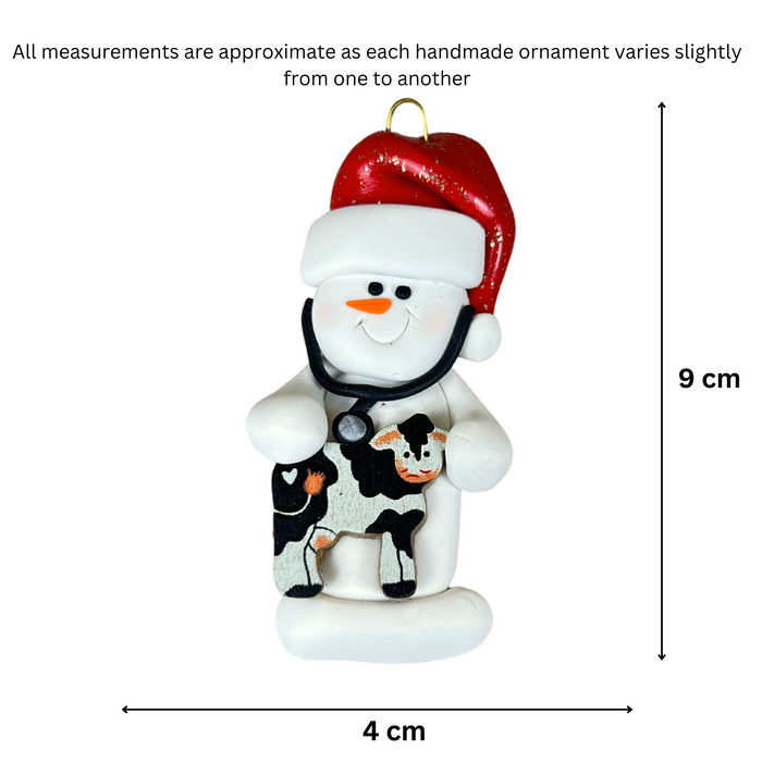 Ornament of white snowman in red hat holding a cow and stethoscope, graphed to show size (4x9cm).
