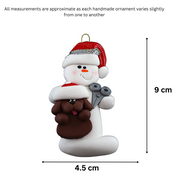 Ornament of white snowman in red hat holding a brown dog and a pair of scissors, graphed to show size (4.5x9cm).