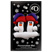A couple’s ornament of two penguins in colourful hats, on display backing card.