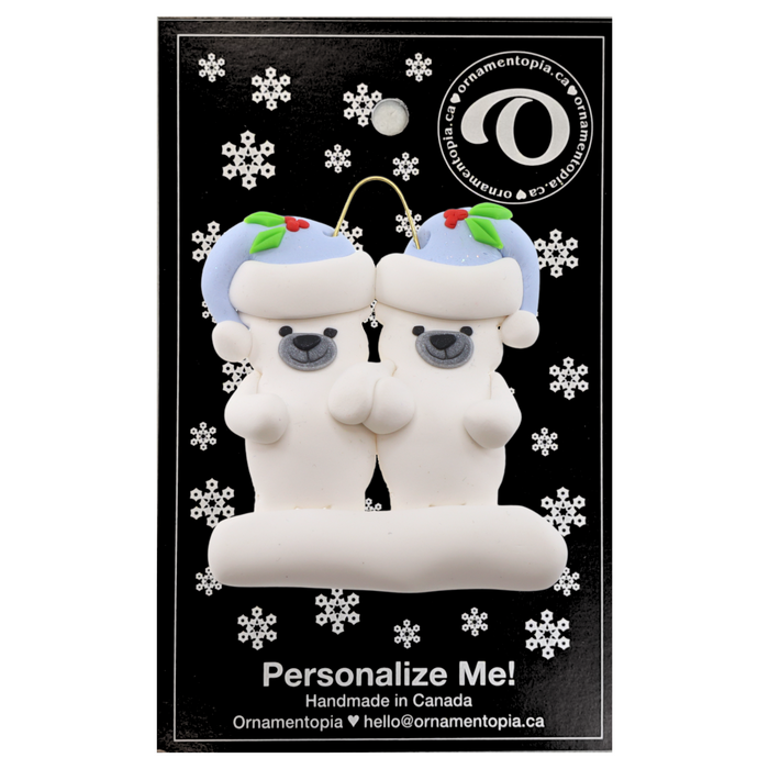 Family ornament with 2 polar bear figures in blue Christmas hats, on display backing card.