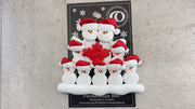 Family ornament with 9 white snowmen in red hats, gathered around a red maple leaf, shown on backing card and Christmas tree.