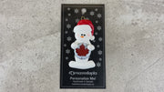 Ornament of white snowman in red hat holding a beer bottle cap, shown on backing card and Christmas tree.