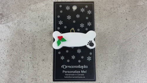 Ornament of dog bone with holly and paw print,shown on backing card and decorated Christmas tree.