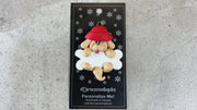 Ornament of tan dog in red hat hanging on a white bone, shown on backing card and Christmas tree.
