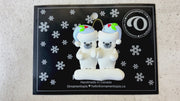 Family ornament with 2 polar bear figures in blue Christmas hats, shown on backing card and Christmas tree.