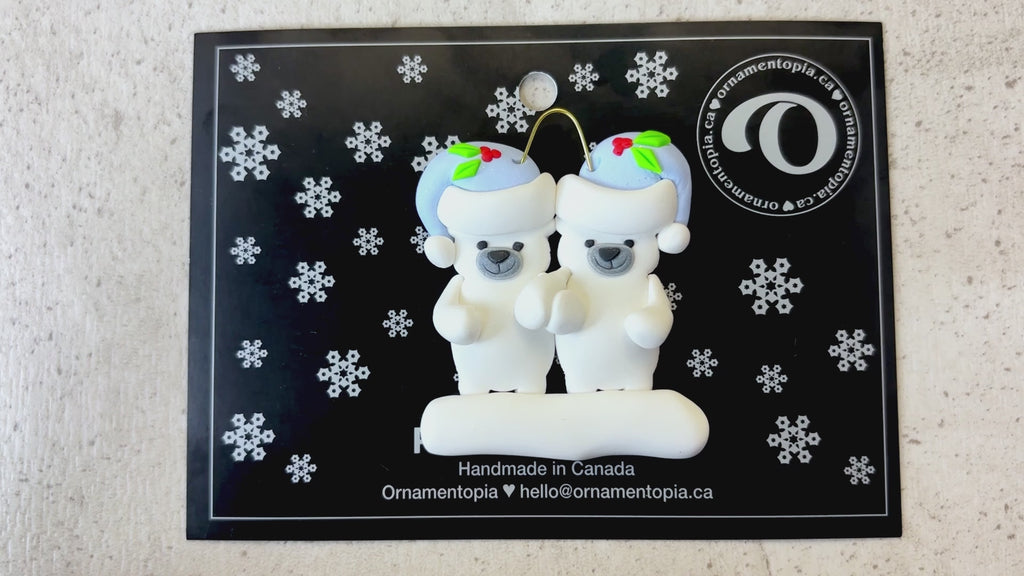 Family ornament with 2 polar bear figures in blue Christmas hats, shown on backing card and Christmas tree.