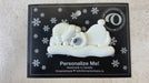 Ornament of white sleeping polar bear baby in a white sparkling hat, shown on backing card and Christmas tree.