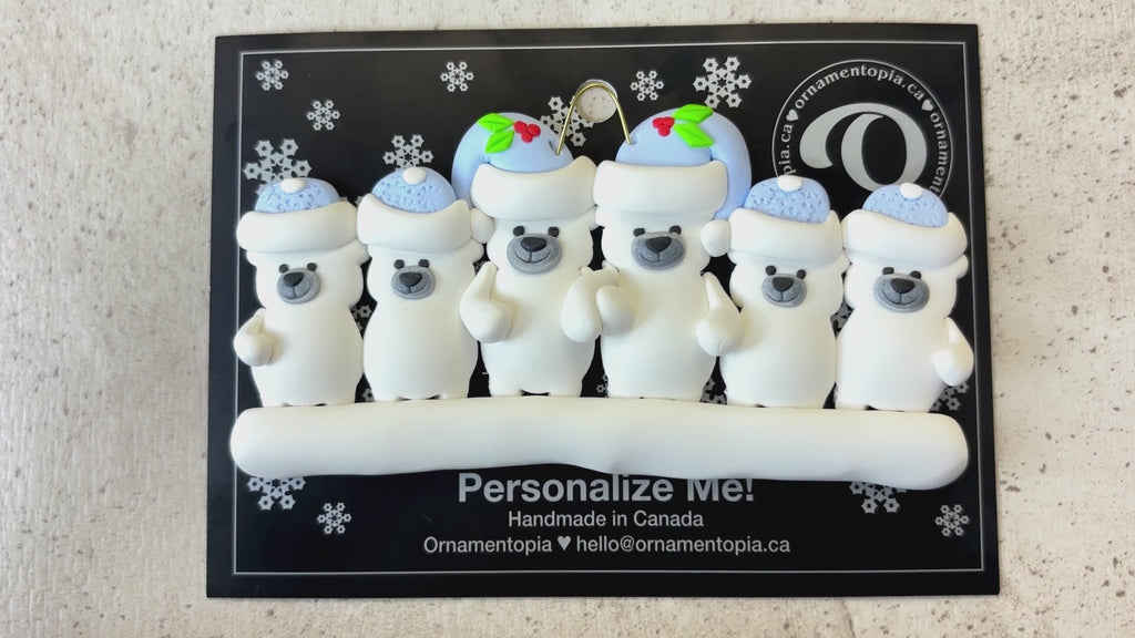 Family ornament with 6 polar bear figures in blue Christmas hats, shown on backing card and Christmas tree.