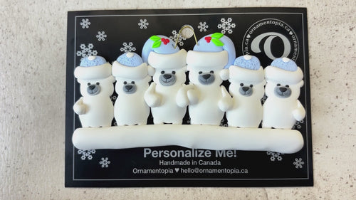 Family ornament with 6 polar bear figures in blue Christmas hats, shown on backing card and Christmas tree.