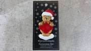 Tan bear in red festive hat with maple leaf ornament, shown on backing card and Christmas tree.