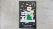 Family ornament with 1 large and 3 small white snowmen in bright scarves, with green Christmas tree, shown on backing card and Christmas tree.
