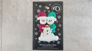 Ornament of snowman couple in red and green shirts and hats with white dog in Christmas hat, shown on backing card and Christmas tree.