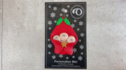 Ornament with triplet infant heads poking out of a red baby blanket, shown on backing card and Christmas tree.