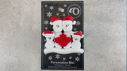 Family ornament with 4 white snowmen in red hats, gathered around a red maple leaf, shown on backing card and Christmas tree.