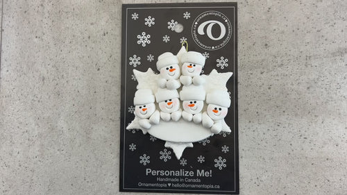 Family ornament with 6 white snowmen stacked on top of a glitter white snowflake, shown on backing card and Christmas tree.