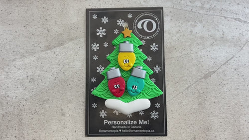 Christmas tree ornament decorated with 3 light bulbs with smiling faces, shown on backing card and decorated Christmas tree.