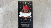 Ornament of brown dog in red hat hanging on a white bone, shown on backing card and Christmas tree.