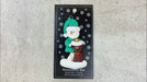 Ornament of snowman in a green shirt and hat with brown cat in Christmas hat, shown on backing card and Christmas tree.
