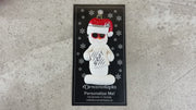 Ornament of white snowman in red hat and sunglasses holding a movie script, shown on backing card and Christmas tree.