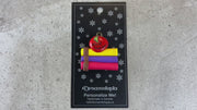 Stack of books and red apple teacher appreciation ornament, shown on backing card and Christmas tree.