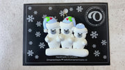 Family ornament with 3 polar bear figures in blue Christmas hats, shown on backing card and Christmas tree.