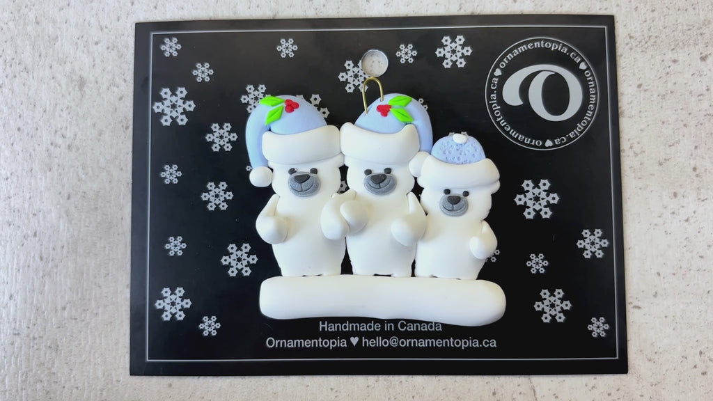 Family ornament with 3 polar bear figures in blue Christmas hats, shown on backing card and Christmas tree.
