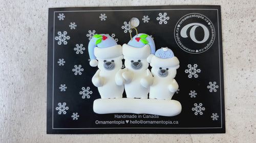 Family ornament with 3 polar bear figures in blue Christmas hats, shown on backing card and Christmas tree.