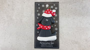 Ornament of black dog in a red and white polka dot Christmas hat and scarf, shown on backing card and Christmas tree.