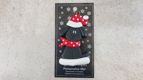 Ornament of black dog in a red and white polka dot Christmas hat and scarf, shown on backing card and Christmas tree.