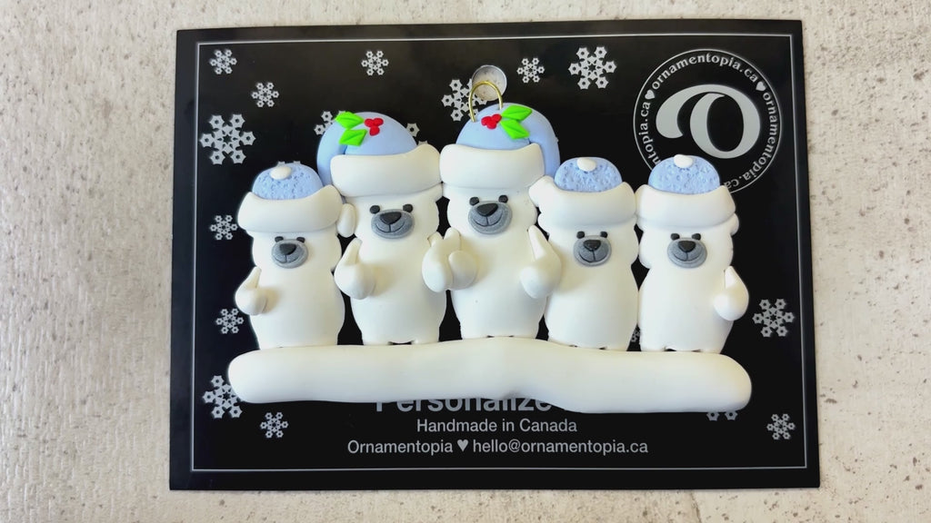 Family ornament with 5 polar bear figures in blue Christmas hats, shown on backing card and Christmas tree.