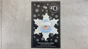 Baby ornament with infant face and blue hat on glittery white snowflake base, shown on backing card and Christmas tree.