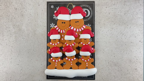 Family ornament with 8 brown gingerbread figures in red Christmas hats, shown on backing card and Christmas tree.