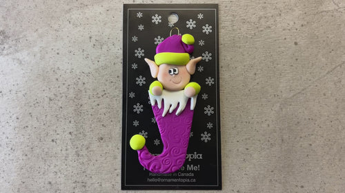 Elf poking out of magenta stocking ornament, shown on backing card and Christmas tree.