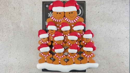 Family ornament with 13 brown gingerbread figures in red Christmas hats, shown on backing card and Christmas tree.
