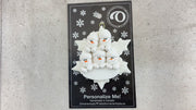 Family ornament with 5 white snowmen stacked on top of a glitter white snowflake, shown on backing card and Christmas tree.